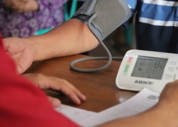 Mężczyzna po pięćdziesiątce mierzy ciśnienie ciśnieniomierzem naramiennym przy kuchennym stole